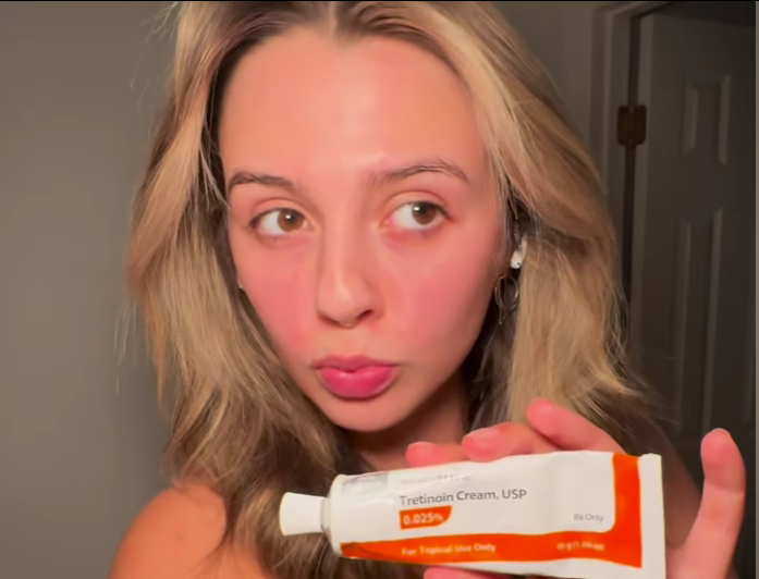 A woman holding a tube of Tretinoin Cream, USP 0.025% in front of the camera.