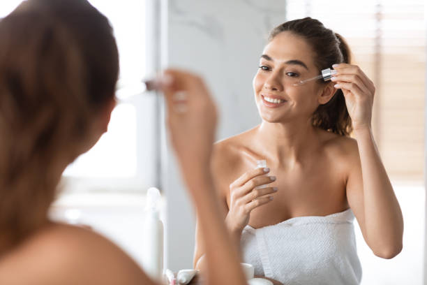 Smiling woman applying facial serum in front of bathroom mirror