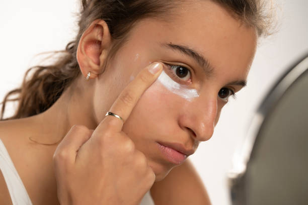 Young woman applying cream under her eyes